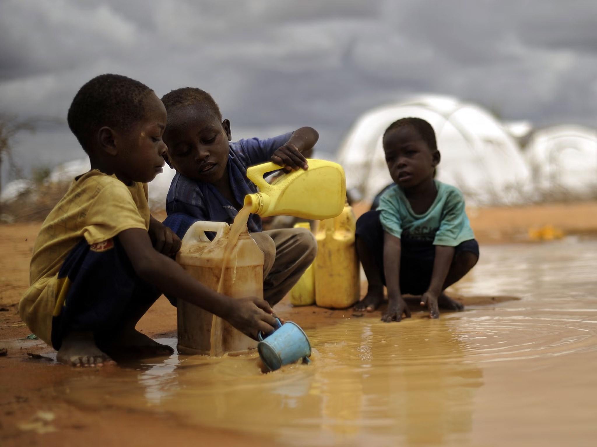 Children collecting unsafe muddy water near aid tents